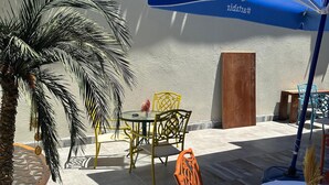 An outdoor patio area with a table and chairs, a blue umbrella, and a palm tree. - Lost town Inn Hotel (Antalya)