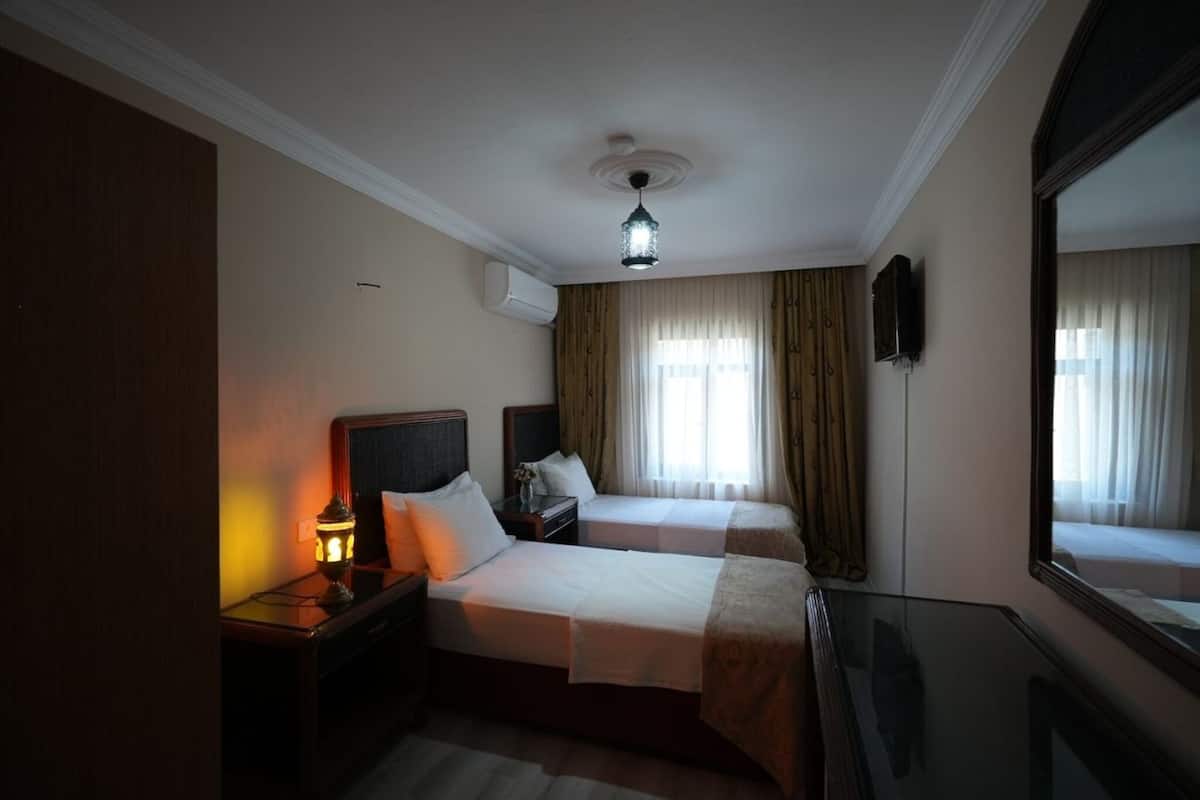A hotel room with two beds, a nightstand, a lamp, a mirror, and a ceiling light fixture.