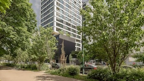 Un moderno edificio de gran altura con fachada de vidrio, rodeado de exuberante vegetación y automóviles estacionados.