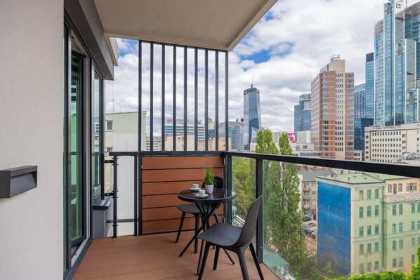 A balcony with a table and chairs, a potted plant, and a city view.