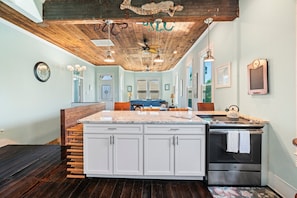 A kitchen with a large island, white cabinets, a dark wooden floor, and a ceiling with exposed beams and pendant lights. - Make new memories at Galvez Cottage (Galveston)