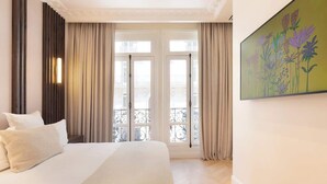 A hotel room with a large bed, a balcony with curtains, and a painting on the wall. - Exceptional 3BR/3BA w/ Services - Champs-Elysées (Paris)