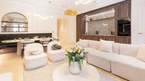 A modern living room with a sofa, a dining area with a table, and a kitchen with wooden cabinets. - Exceptional 3BR/3BA w/ Services - Champs-Elysées (Paris)