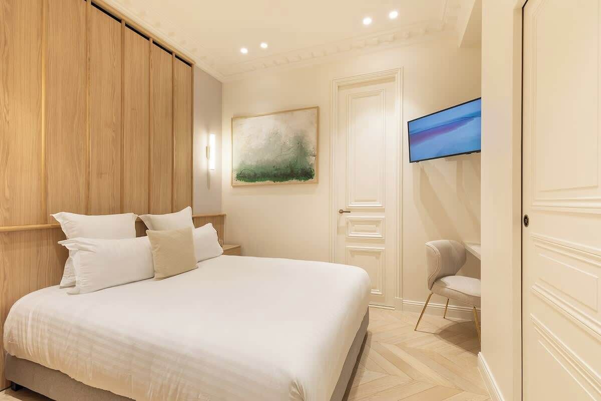 A bedroom with a large bed, a wooden panel wall, a painting, a television, and a chair.