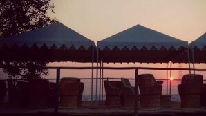A sunset view with three tents and lounge chairs facing the water. - KUMBH CAMP OM (Karchana)