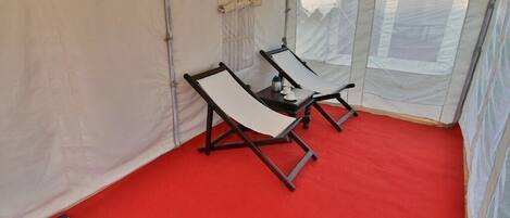 A tent with two reclining chairs and a small table with a bottle and cup.