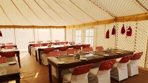 A tented dining area with multiple tables and chairs, each set with plates, cutlery, and glasses. - KUMBH CAMP OM (Karchana)