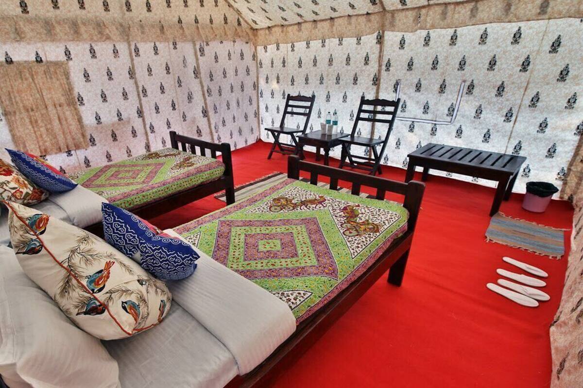 A tent-style room with two beds, each with patterned bedding and pillows, a small table, and chairs.
