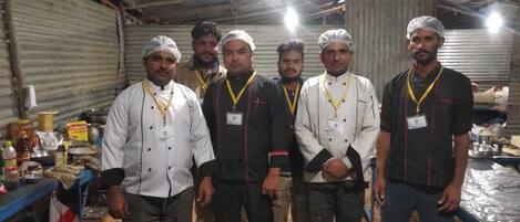 A group of chefs in a kitchen with stainless steel pots and cooking utensils.