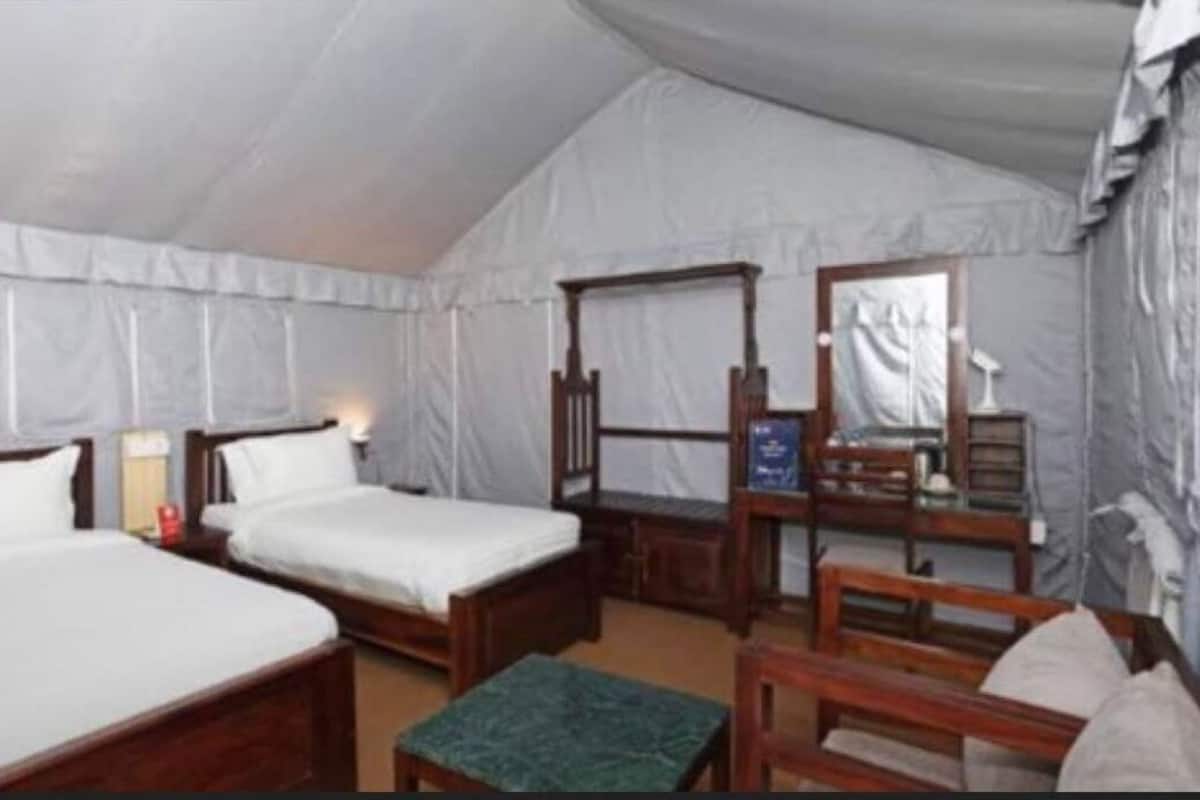 A tented room with two single beds, a wooden chair, and a small table.