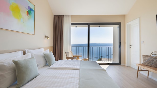 Une chambre d’hôtel avec un grand lit, une vue sur la mer et un balcon équipé d’une chaise.