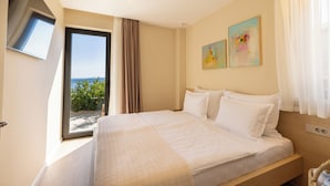 Une chambre avec un grand lit, une fenêtre donnant sur la mer et deux tableaux abstraits accrochés au mur.