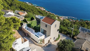 Une maison moderne dotée d’une petite terrasse et d’une piscine, entourée d’une végétation luxuriante et offrant une vue sur la côte.