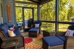 A covered outdoor seating area with wicker furniture, a patterned rug, and a view of a lake.