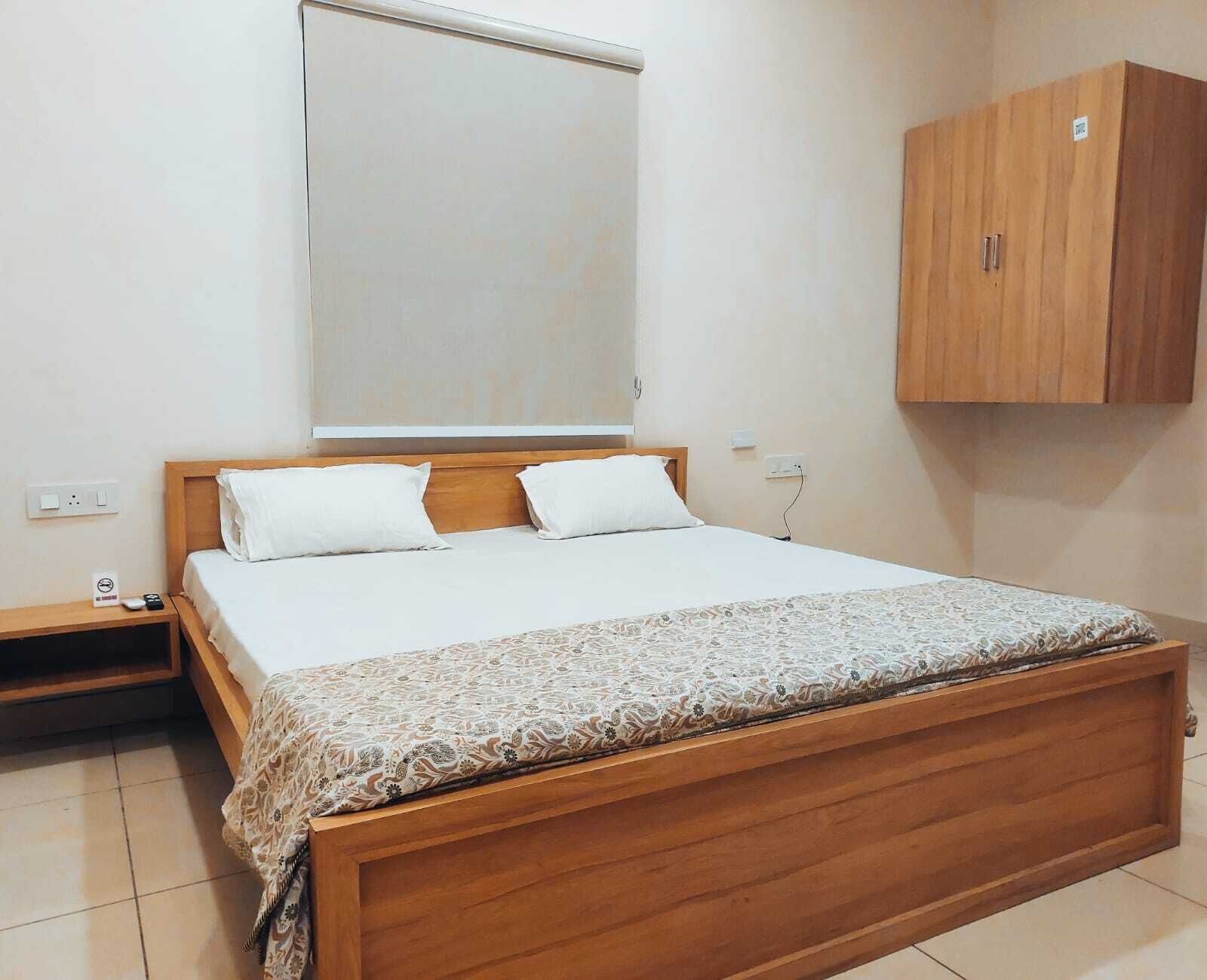 A bedroom with a wooden bed, white bedding, a wooden nightstand, a wooden wardrobe, and a large mirror on the wall.