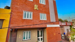 A multi-story building with a prominent 'RAJVI RESIDENCY' sign. It features a brick facade, multiple windows, and a central entrance with a red carpet. - Hotel Rajvi Residency A Unit of JAS Hotels & Resorts (Bikaner)