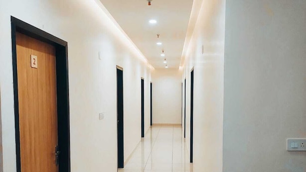 A hallway with a wooden door labeled '2', a potted plant, and a light switch on the wall. - Hotel Rajvi Residency A Unit of JAS Hotels & Resorts (Bikaner)