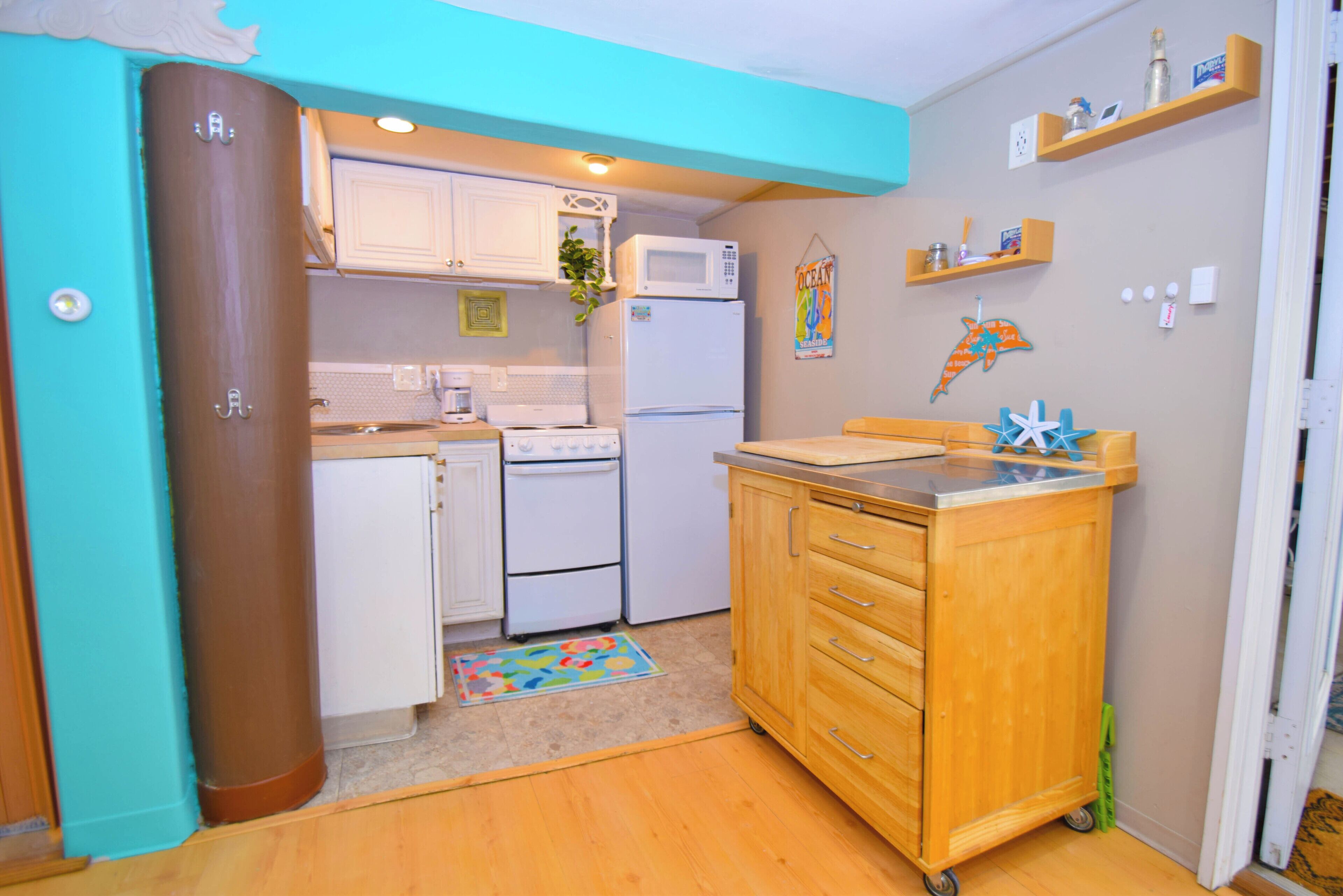 A compact kitchen with white appliances, a wooden cabinet, and a colorful rug.