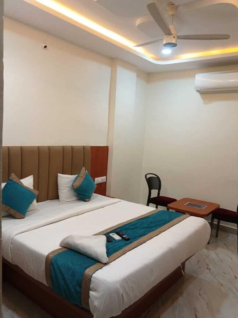 A hotel room with a bed, a small table, a chair, a ceiling fan, and an air conditioning unit.