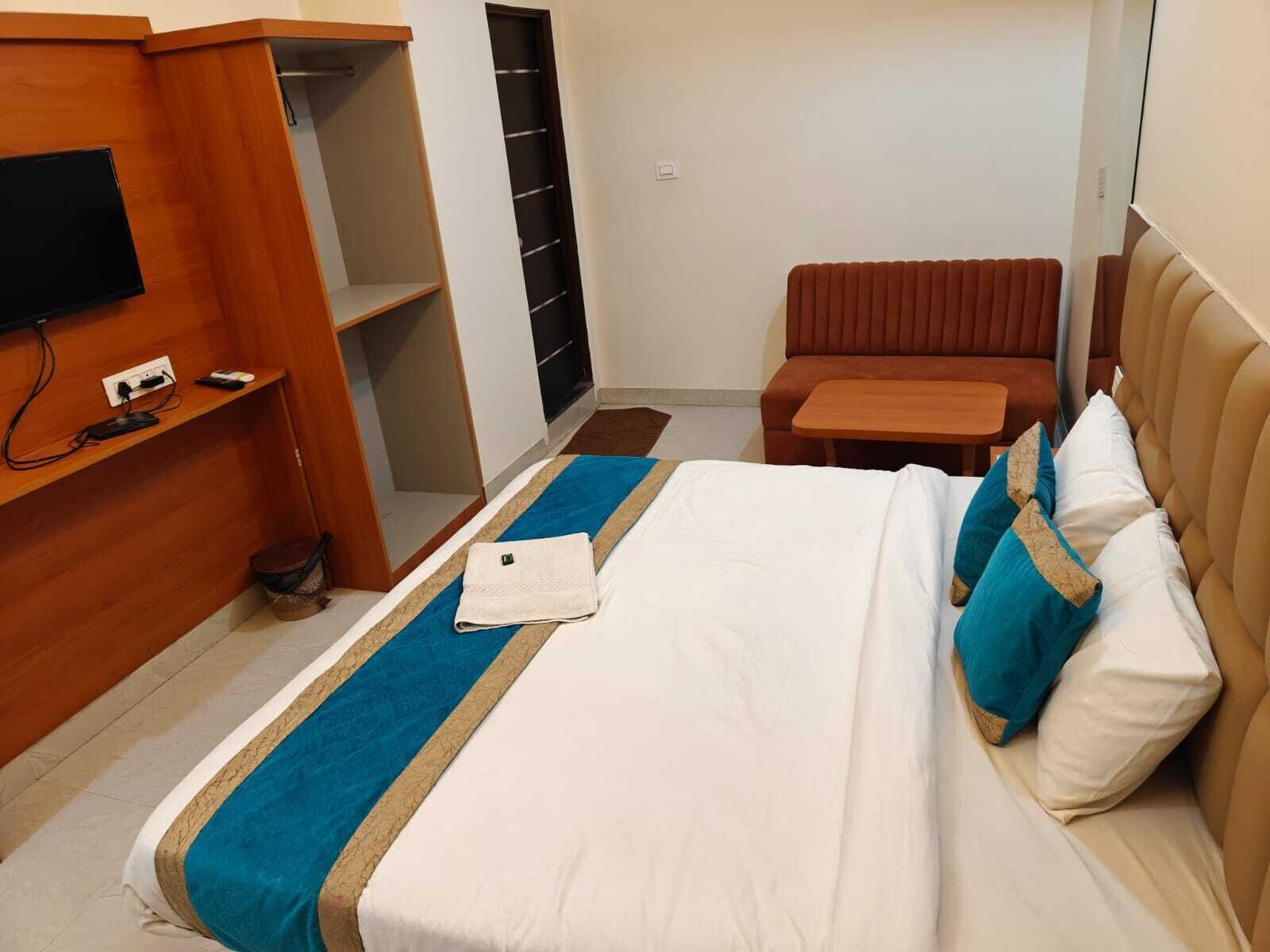 Ett hotellrum med en säng, en tv som är monterad på väggen, ett litet bord och en sittgrupp.