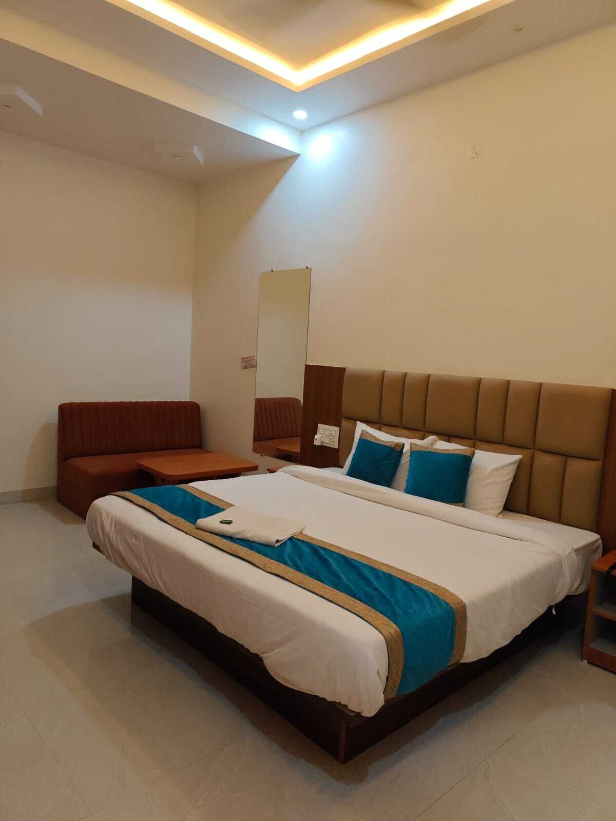 A hotel room with a large bed, a wooden headboard, a bedside table, a nightstand, a seating area with a bench, and a mirror on the wall.