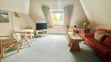 Ein gemütliches Wohnzimmer mit Fernseher, einem Esstisch, einem roten Sofa und einem Fenster mit Vorhängen.