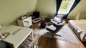 Une petite pièce comprenant un lit, un bureau, une chaise, un téléviseur et une fenêtre avec des rideaux.