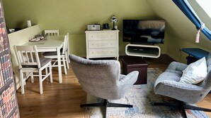 Une pièce confortable de style loft, comprenant une table à manger, deux fauteuils, un téléviseur et une commode.