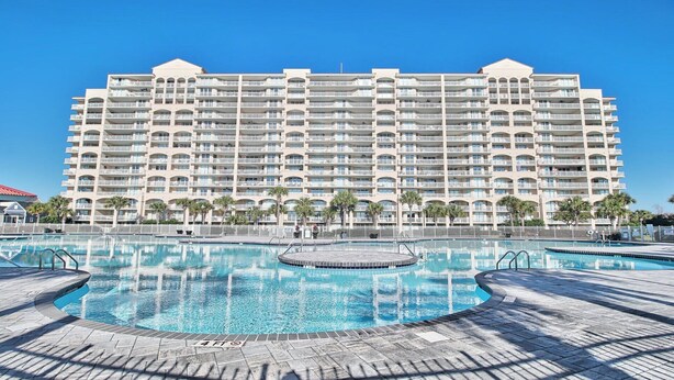 A large hotel with multiple balconies, a central swimming pool, and palm trees. - 3203 Yacht Club Villas (North Myrtle Beach)