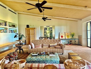 A cozy living room with a striped sofa, a coffee table with books, a ceiling fan, and a bookshelf filled with books. - Maniero in Maremma, luxury villa  in Tuscany (Montiano)