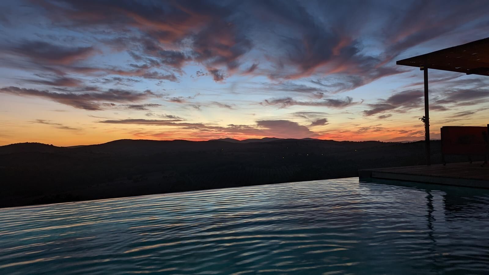 En infinitypool med utsikt över ett bergigt landskap och en solnedgångshimmel.