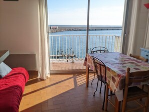 Enjoy a serene view of the water from the balcony, featuring a comfortable bed and a stylish table setting.