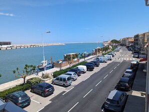 Una calle costera con autos estacionados, un muelle al fondo y edificios a lo largo de la vía.