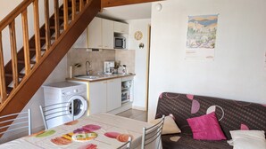 Une cuisine compacte équipée d’un lave-linge, un coin repas avec une table et des chaises, et un canapé à motifs à pois.