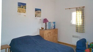 Une chambre à coucher avec un lit, une commode en bois, une lampe et deux affiches au mur.