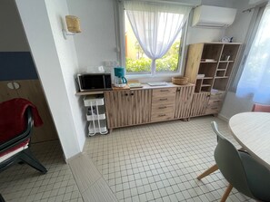 Compact kitchen area with microwave and coffee maker, featuring a shelf unit with storage space and a small window.