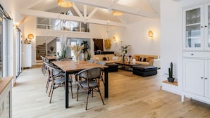 A spacious living area with a high ceiling, wooden flooring, and a dining table with chairs. There are sofas and a coffee table, and the room has a modern, open design. - Luxurious Villa: Pool, Spa, Gym, Cinema, Near Beach, Sleeps 14 (La Turballe)