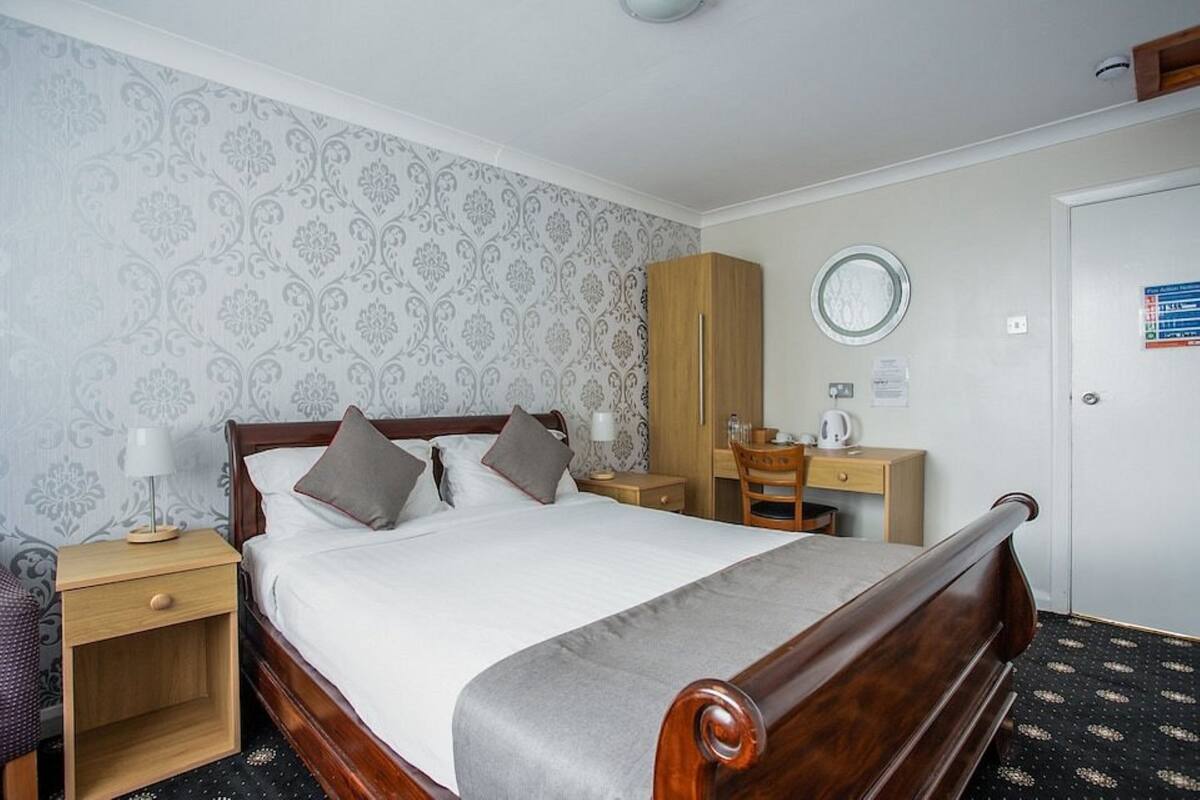 Ein ordentlich eingerichtetes Hotelzimmer mit einem hölzernen Bett, einem Schreibtisch, einem Stuhl und einem Kleiderschrank.