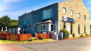 A two-story building with a stone facade, a sign for 'OYO Knowsgate Hotel', and a red fence with potted plants. - Knowesgate Hotel (Newcastle-upon-Tyne)