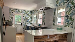 A modern kitchen with a large island, wooden bar stools, and a view of the outdoors through windows. - Walkable neighborhood! The Sun House - Entire home to yourself (Atlanta)