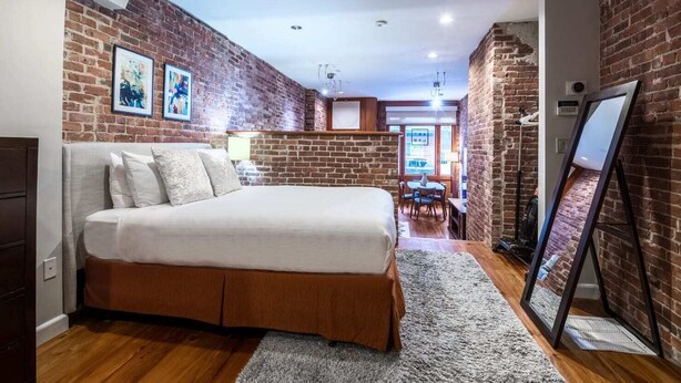 Un dormitorio con pared de ladrillo, una cama, un escritorio y una silla.