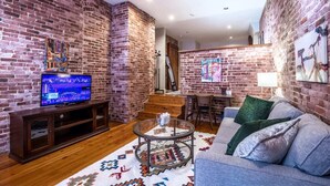 Una sala de estar con pared de ladrillo, televisor, sofá, mesa de centro y alfombra estampada.