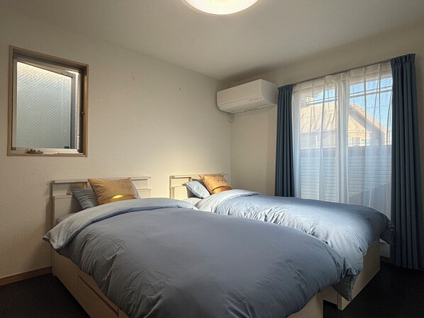 Una habitación con dos camas, una ventana con cortinas, un equipo de aire acondicionado y un espejo en la pared.