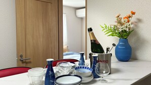 Une pièce avec une porte en bois, une table dressée avec de la vaisselle bleue et blanche, un vase bleu rempli de fleurs et une bouteille de champagne.