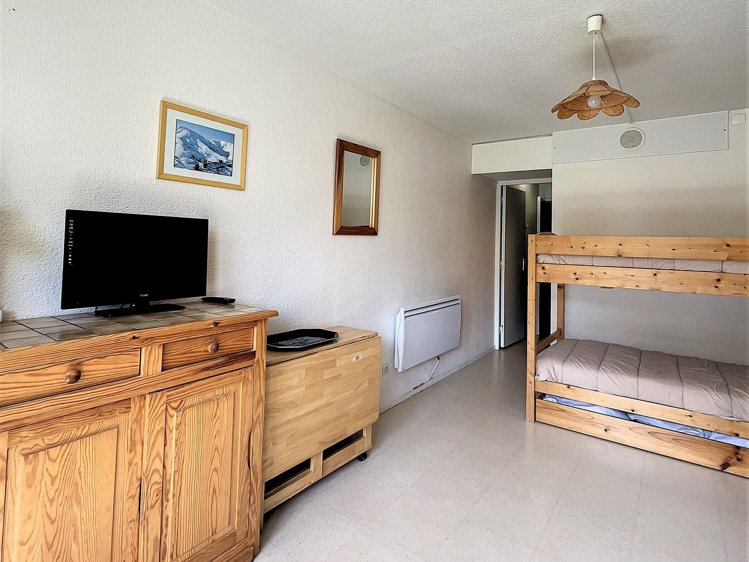 Une pièce comprenant une commode en bois, un téléviseur, un lit superposé, un radiateur et un tableau encadré accroché au mur.