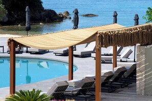 Un espace aménagé au bord de la piscine, avec des chaises longues, un auvent en corde et une vue sur la mer.