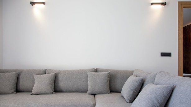 A modern living room with a grey sectional sofa, two wall-mounted lights, and a small black table. - Arete Lifestyle Hotel (Igoumenitsa)
