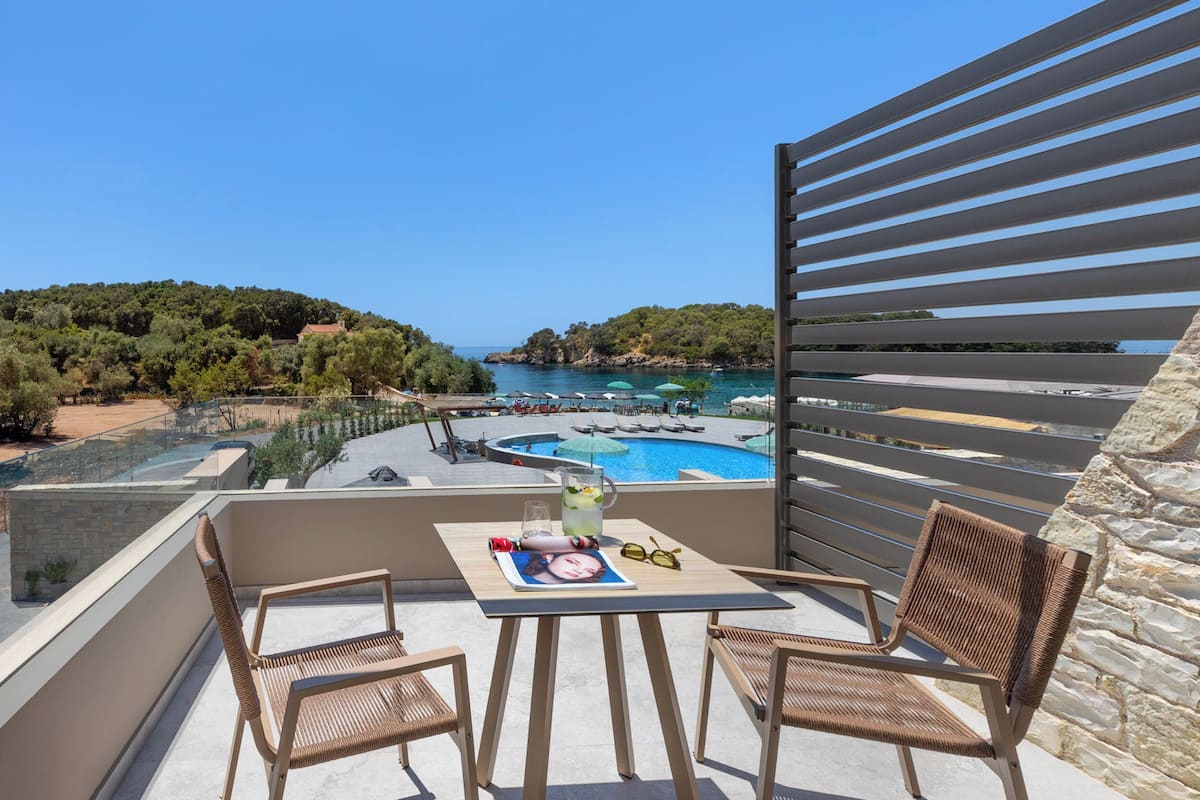 Un balcó amb una taula, dues cadires de vimetes i vista a una piscina i una platja.