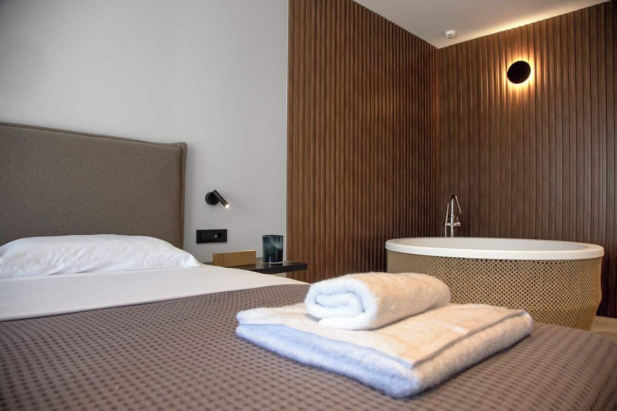 Habitació d'hotel moderna amb un llit gran, una banyera rodona i panells de paret de fusta.