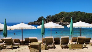 A beach with wooden lounge chairs and white umbrellas. - Arete Lifestyle Hotel (Igoumenitsa)